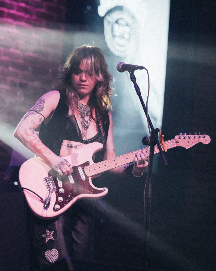 Guitar and vocals at the mic on a brick-wall stage